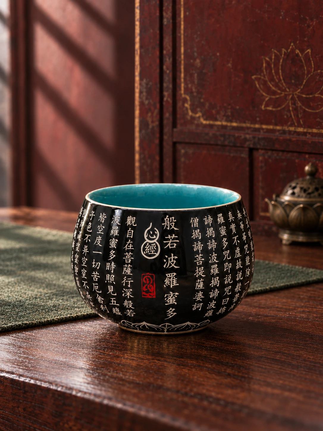 Black Heart Sutra cup with a turquoise interior beside muted green linen and a bronze lotus incense burner