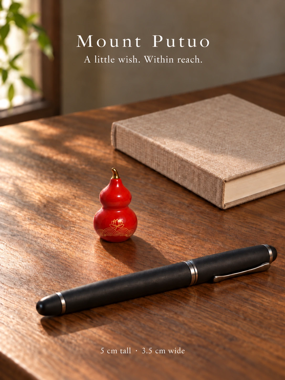 A miniature ceramic gourd beside a pen and book on a wooden desk; 5 cm high and 3.5 cm wide